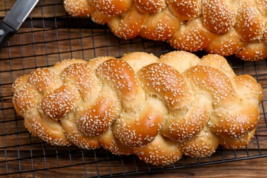 Photo of Homemade braided breads with cooling rack on wooden table, flat lay. Traditional Shabbat challah