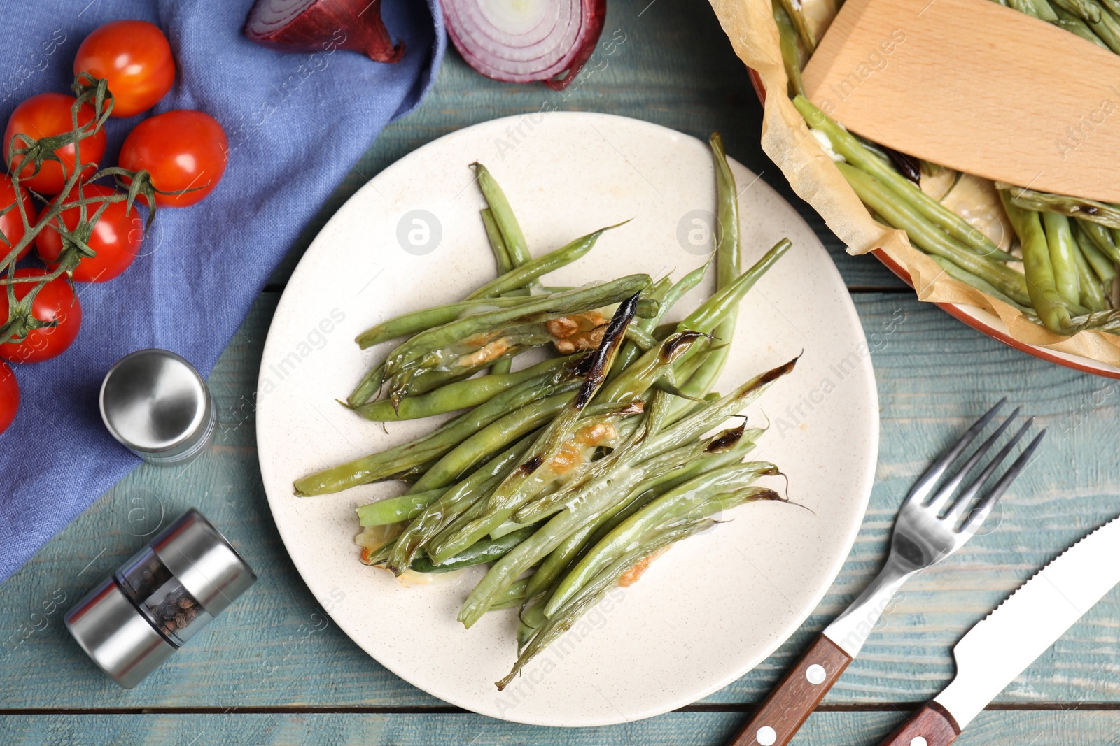 Photo of Delicious baked green beans served on light blue wooden table, flat lay