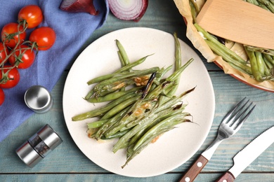 Photo of Delicious baked green beans served on light blue wooden table, flat lay