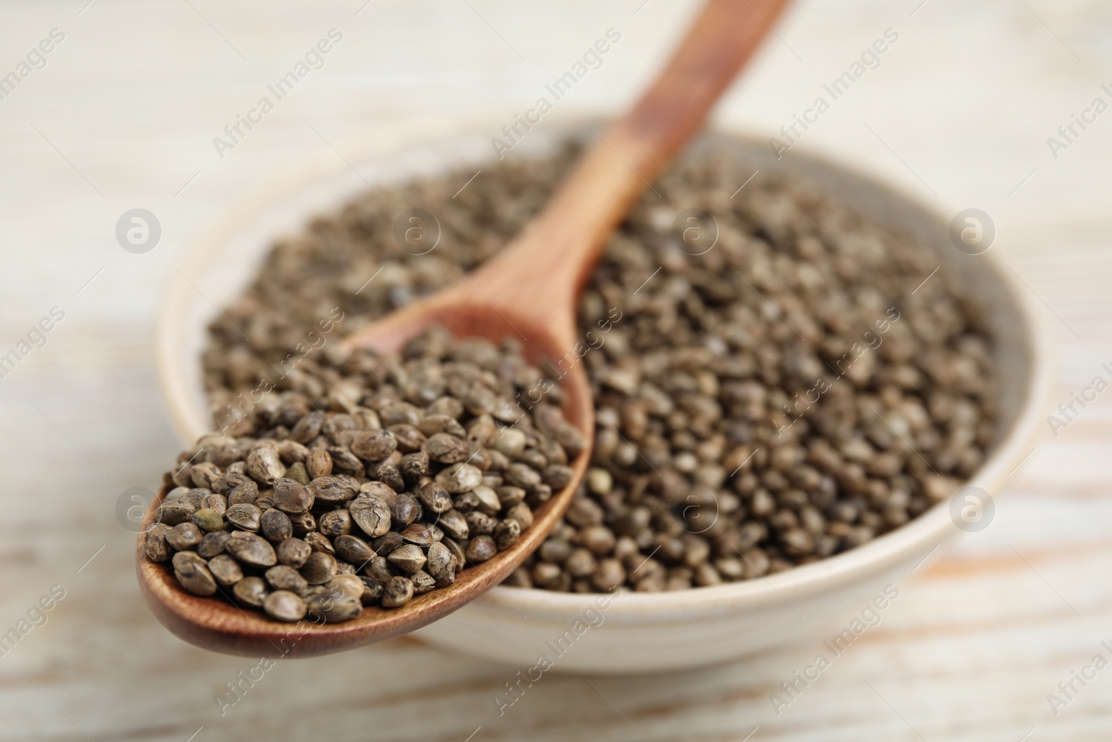 Photo of Bowl and spoon with organic hemp seeds on white table, closeup