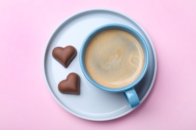 Photo of Romantic breakfast with cup of coffee and chocolate candies on pink background, top view. Valentine's day celebration