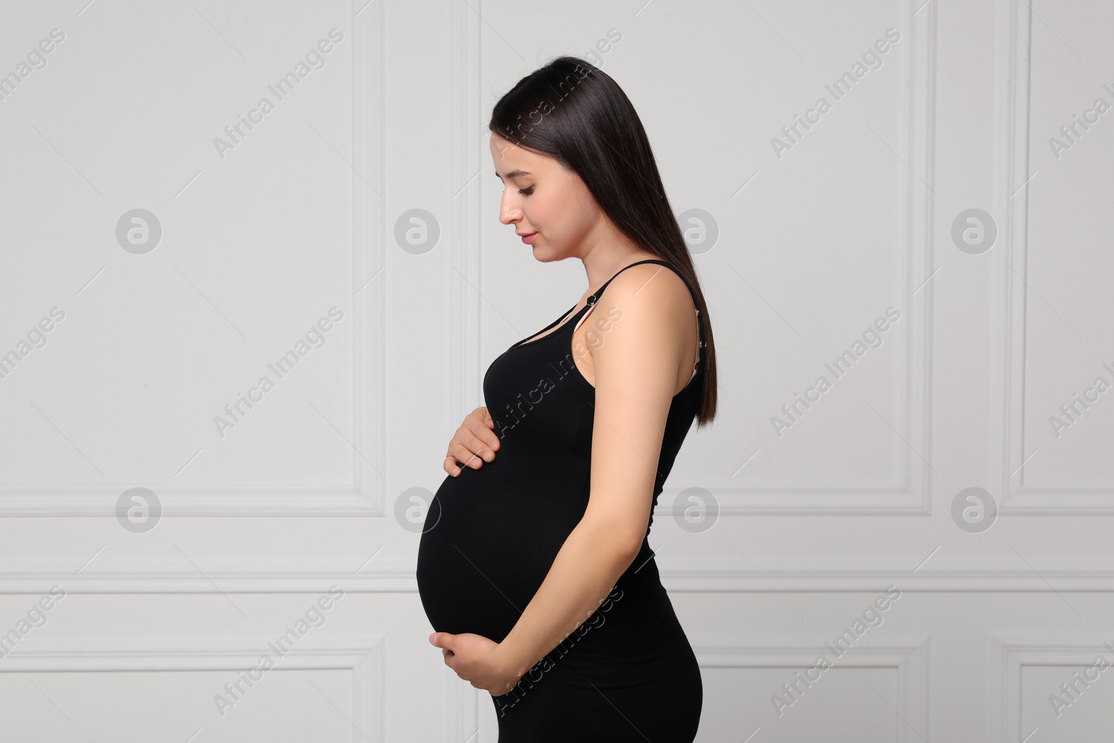 Photo of Beautiful pregnant woman in black dress near light grey wall