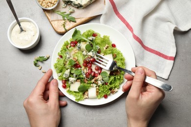Photo of Woman eating fresh salad with pear at grey table, top view