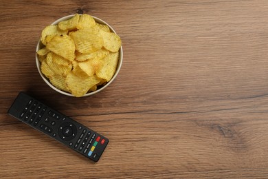 Photo of Modern tv remote control and chips on wooden table, flat lay. Space for text