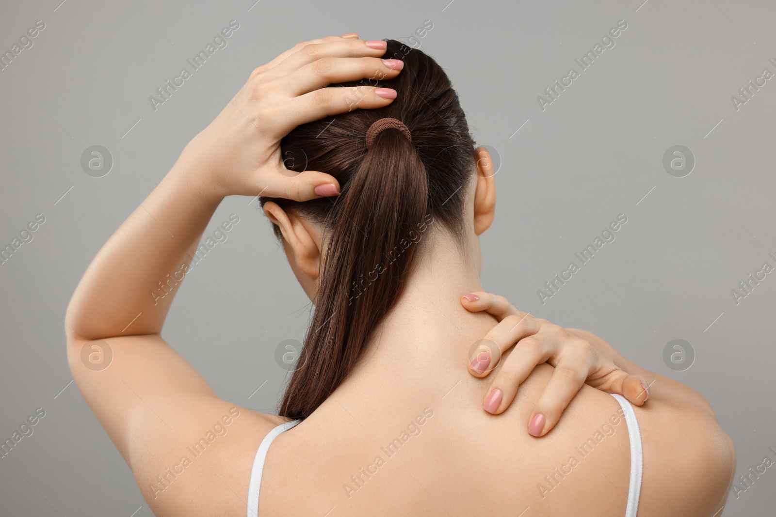 Photo of Woman touching her neck and head on grey background, back view