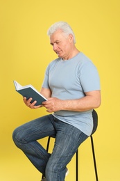 Senior man reading book on color background