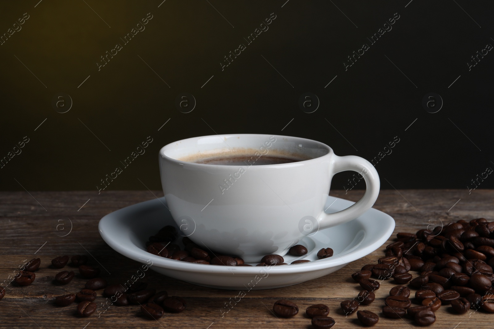 Photo of Cup of hot aromatic coffee and roasted beans on wooden table against dark background