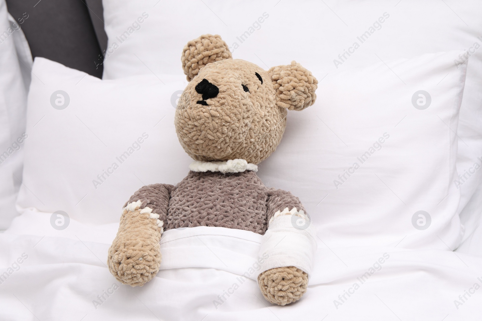 Photo of Toy cute bear with bandage under blanket in bed