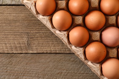Fresh raw chicken eggs in carton on wooden table, top view. Space for text