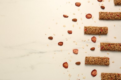 Photo of Tasty granola bars and dried strawberries on white marble table, flat lay. Space for text