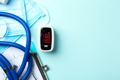 Photo of Flat lay composition with modern fingertip pulse oximeter and medical items on light blue background. Space for text