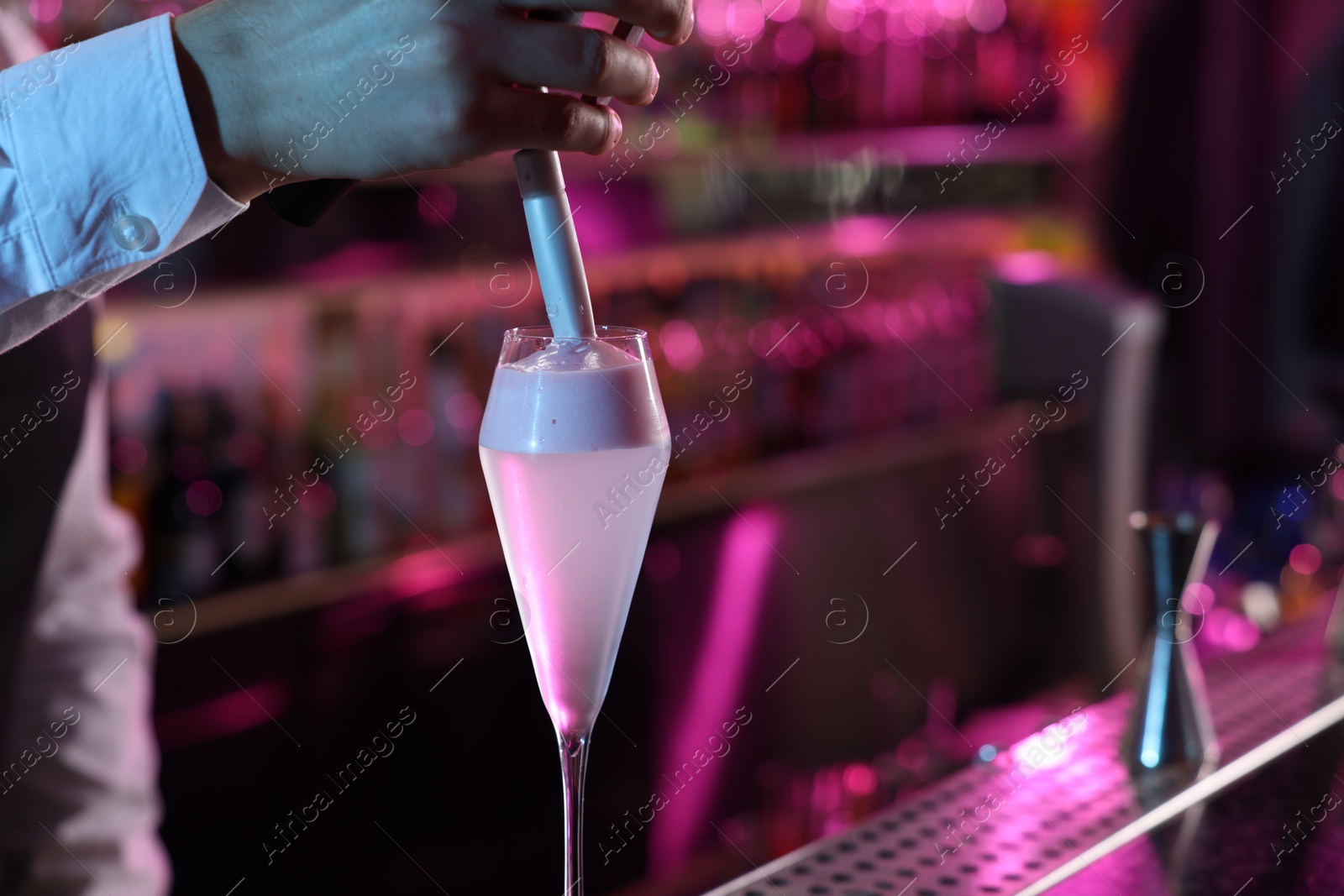 Photo of Bartender adding foam onto alcoholic cocktail at counter in bar, closeup. Space for text