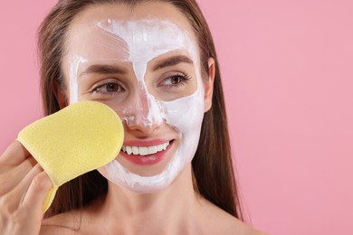 Photo of Happy young woman washing off face mask with sponge on pink background