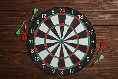 Dart board with color arrows on wooden background, top view