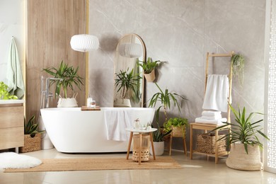 Modern white tub and beautiful green houseplants in bathroom. Interior design