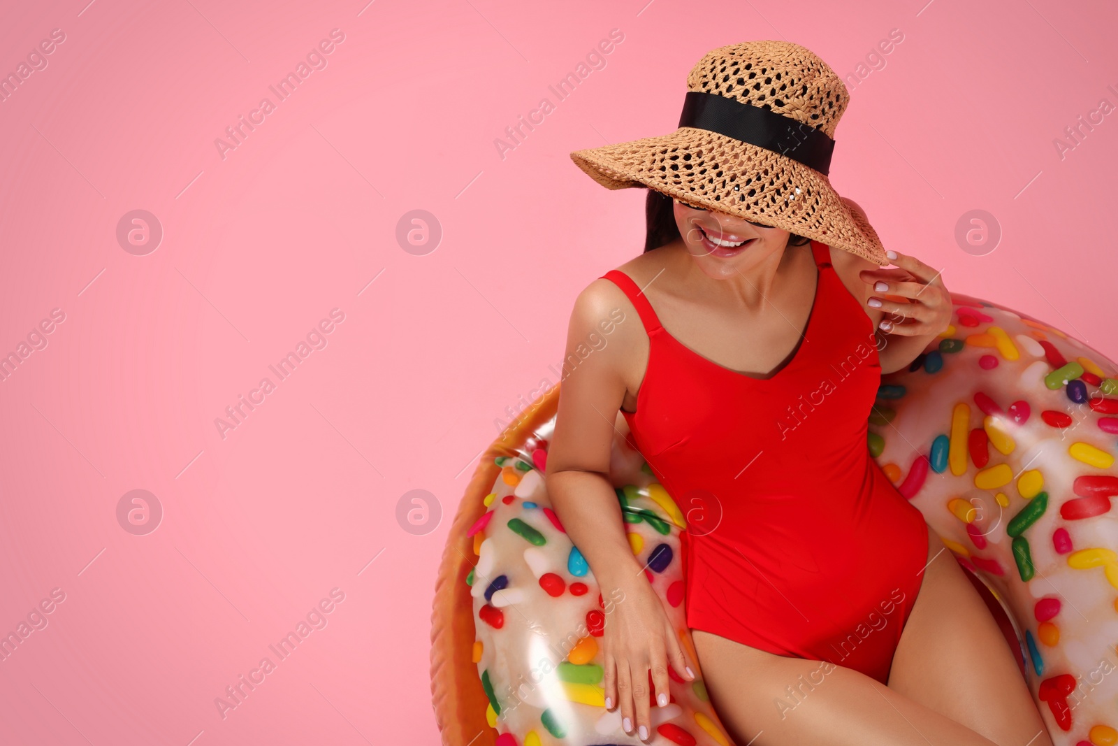 Photo of Young woman in stylish swimsuit on inflatable ring against pink background. Space for text