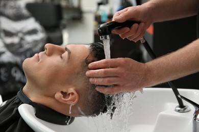 Photo of Professional barber washing client's hair at sink in salon, closeup
