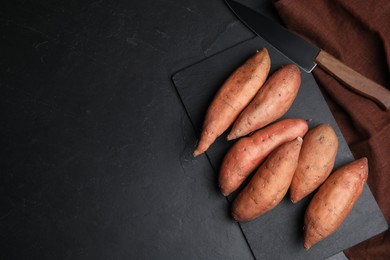 Photo of Heap of whole ripe sweet potatoes on black table, flat lay. Space for text