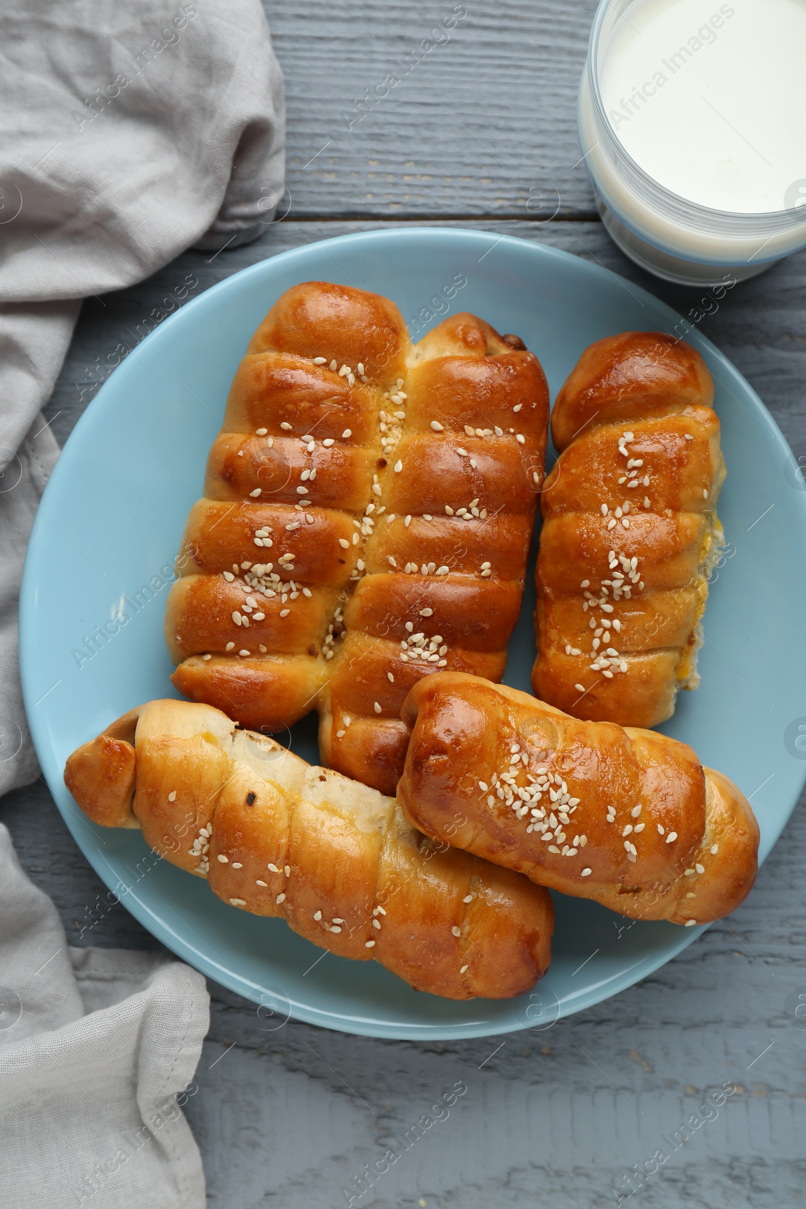 Photo of Delicious sausage rolls and milk on grey wooden table, flat lay