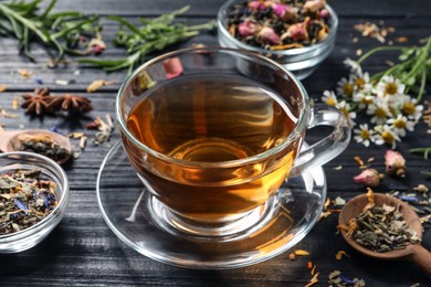 Photo of Composition with freshly brewed tea and different leaves on black wooden table, closeup