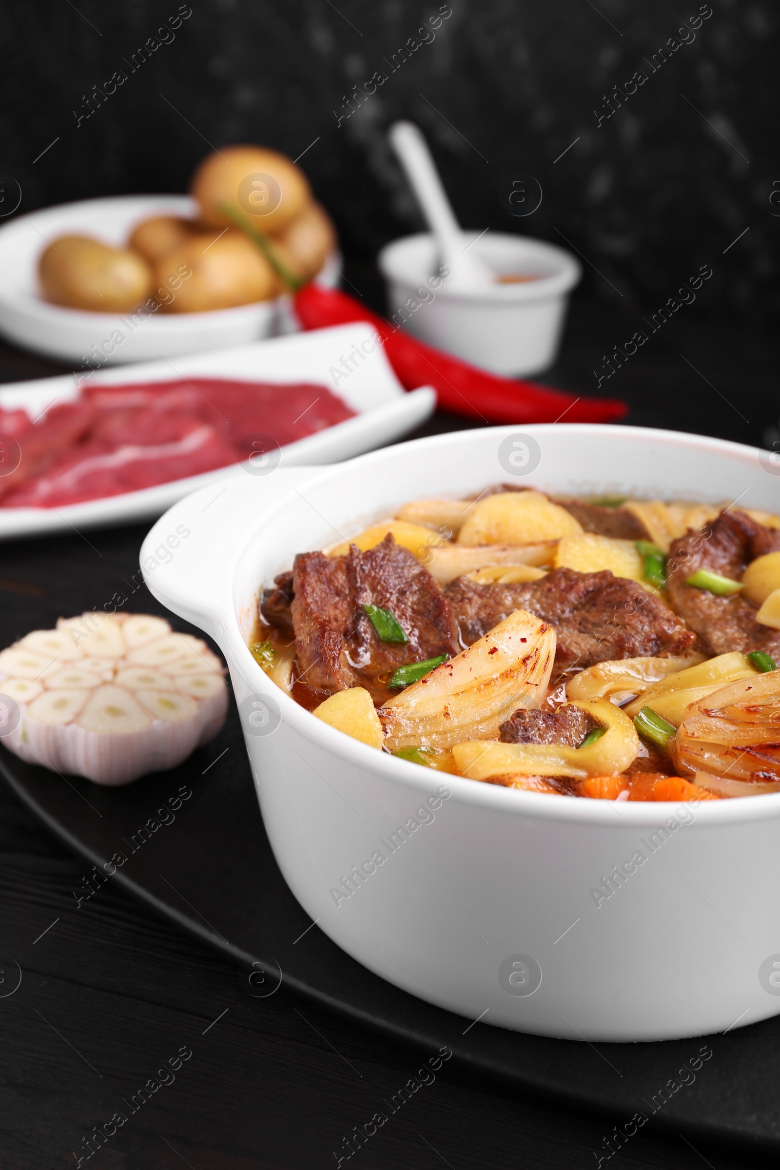 Photo of Pot of delicious vegetable soup with meat, noodles and ingredients on black wooden table, closeup