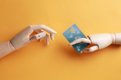 Photo of Wooden mannequin hands with credit card on orange background, flat lay