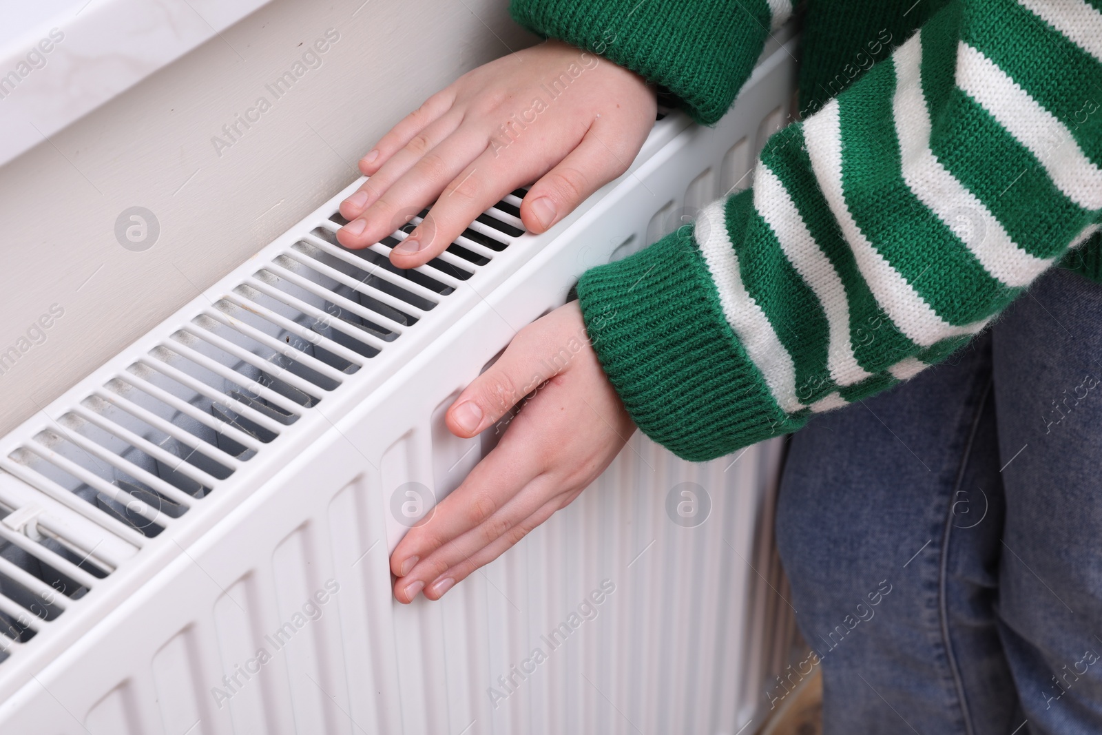 Photo of Girl warming hands on heating radiator indoors, closeup