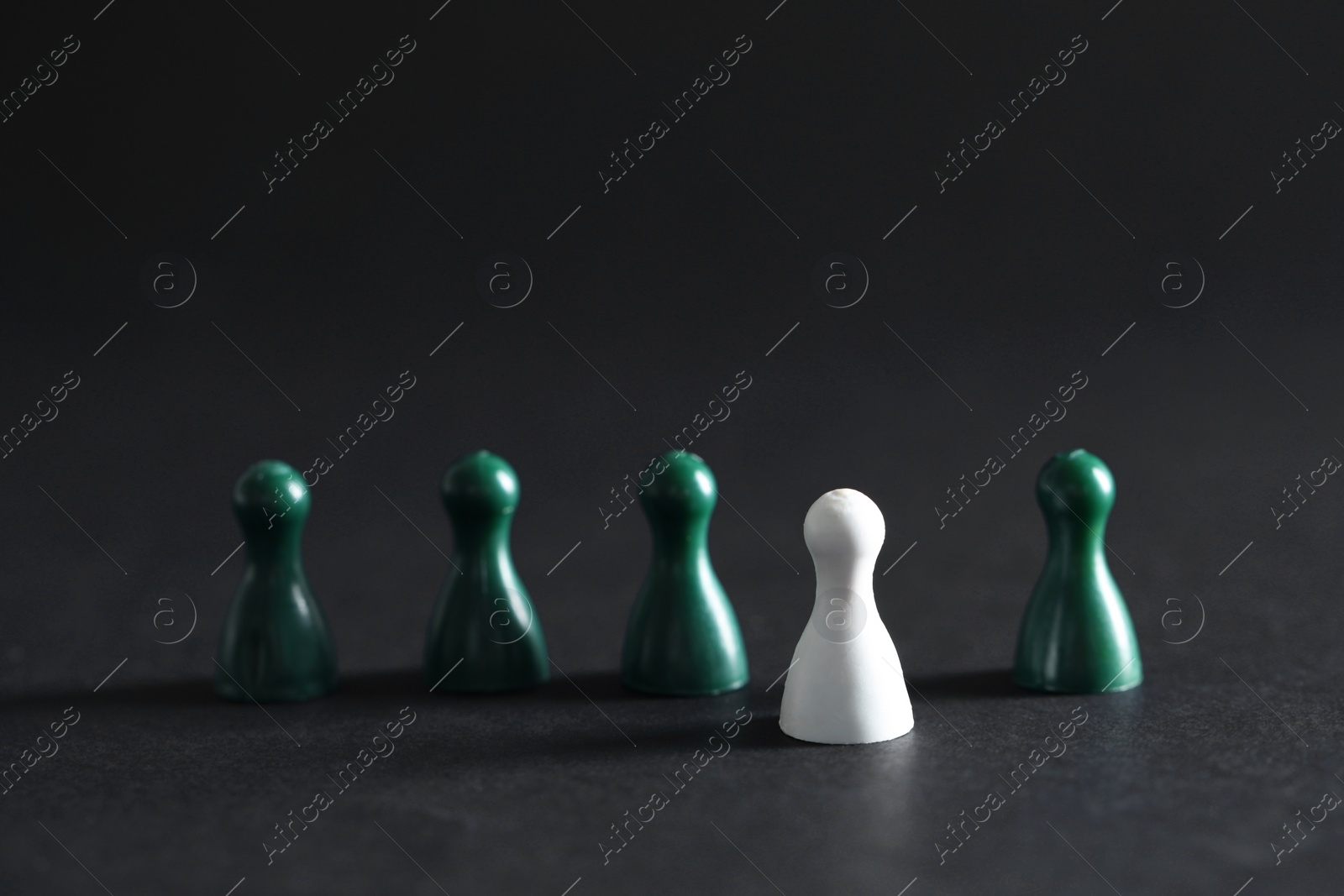 Photo of Choice concept. White pawn and green ones on dark table