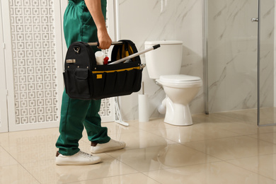 Photo of Professional plumber with toolbox near toilet bowl in bathroom, closeup