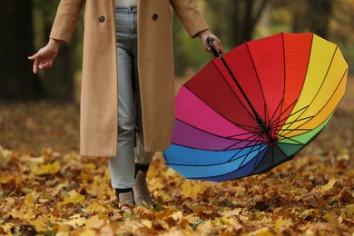 Photo of Woman with rainbow umbrella walking in autumn park, closeup