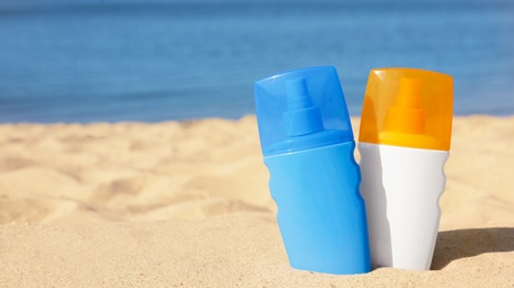 Bottles of sunblock in beach sand near sea. Space for text