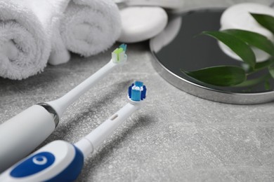 Photo of Electric toothbrushes, rolled towels and leaves on grey textured table, closeup. Space for text