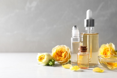 Photo of Bottles of rose essential oil and fresh flowers on table, space for text