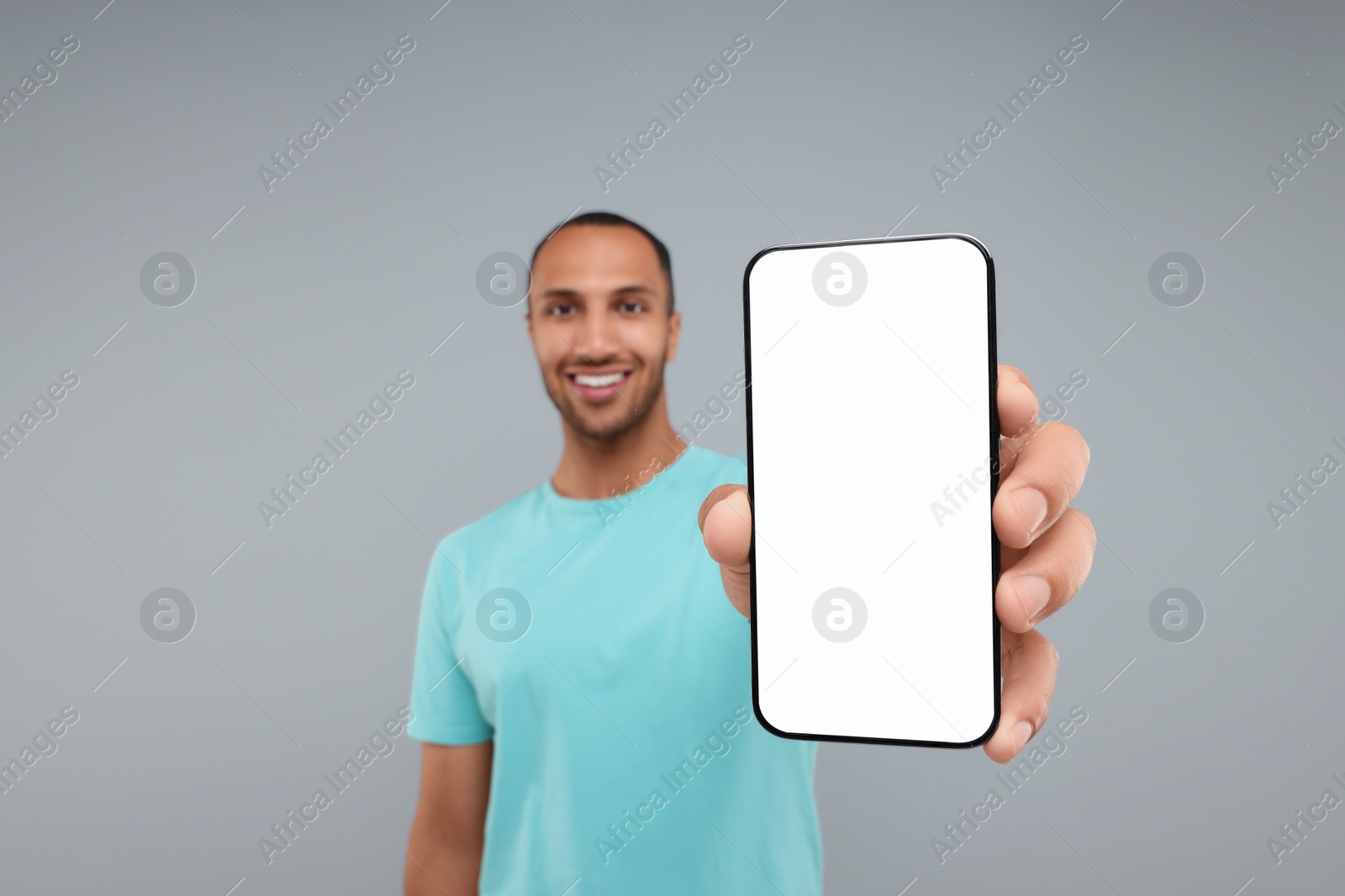 Photo of Young man showing smartphone in hand on light grey background, selective focus. Mockup for design