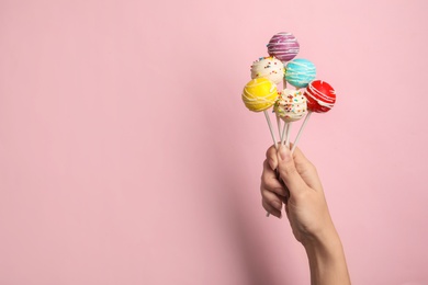 Woman holding bright delicious cake pops on color background, closeup. Space for text