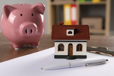 House model, piggy bank, clipboard and pen on wooden table indoors