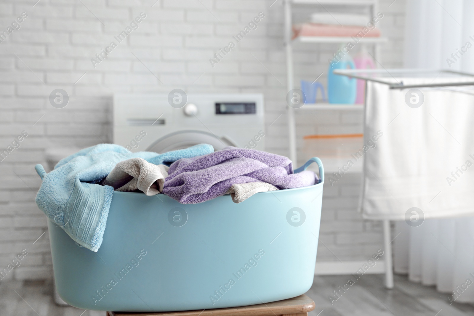 Photo of Plastic basket with dirty towels on table in laundry room