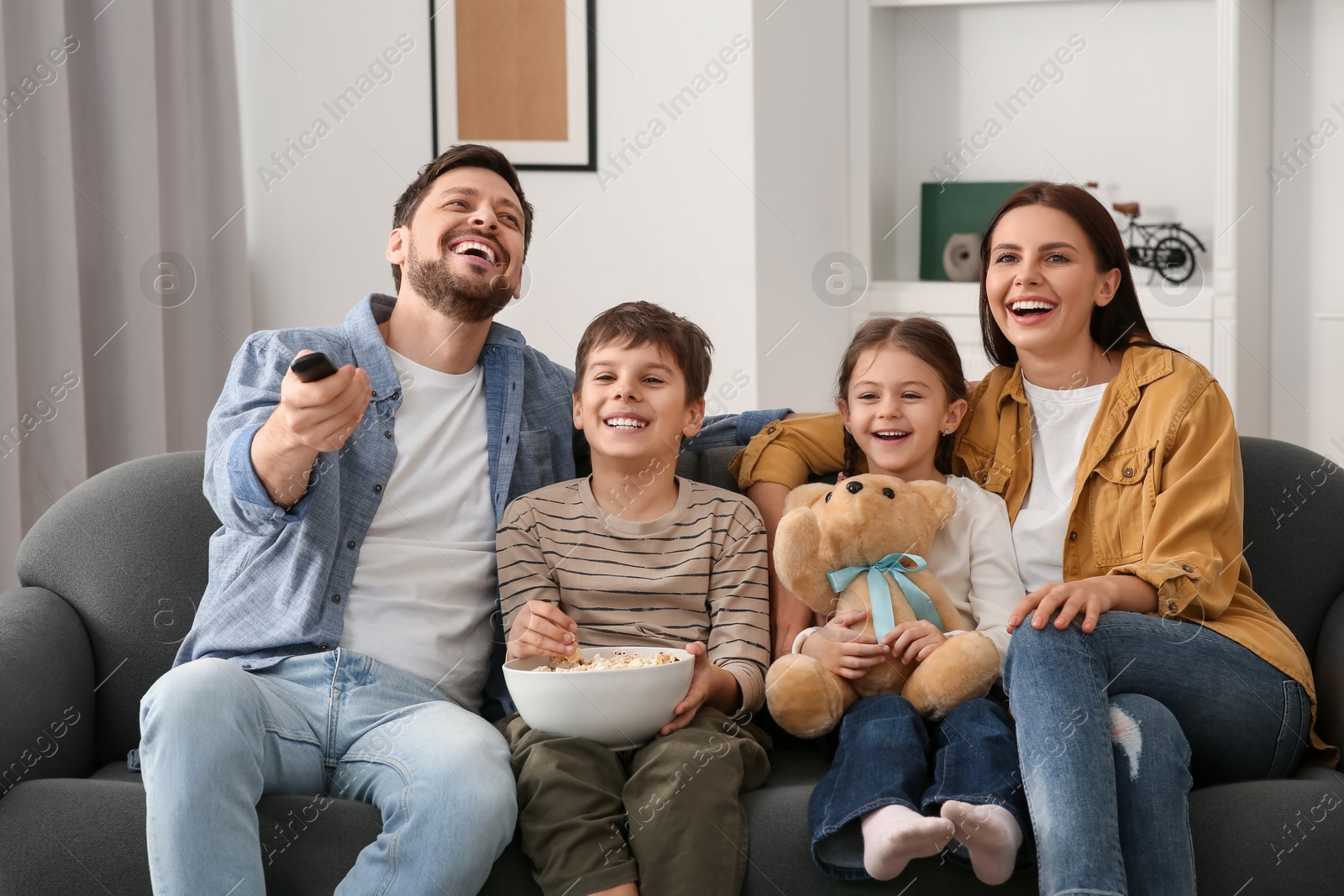 Photo of Happy family watching TV at home. Father changing channels with remote control