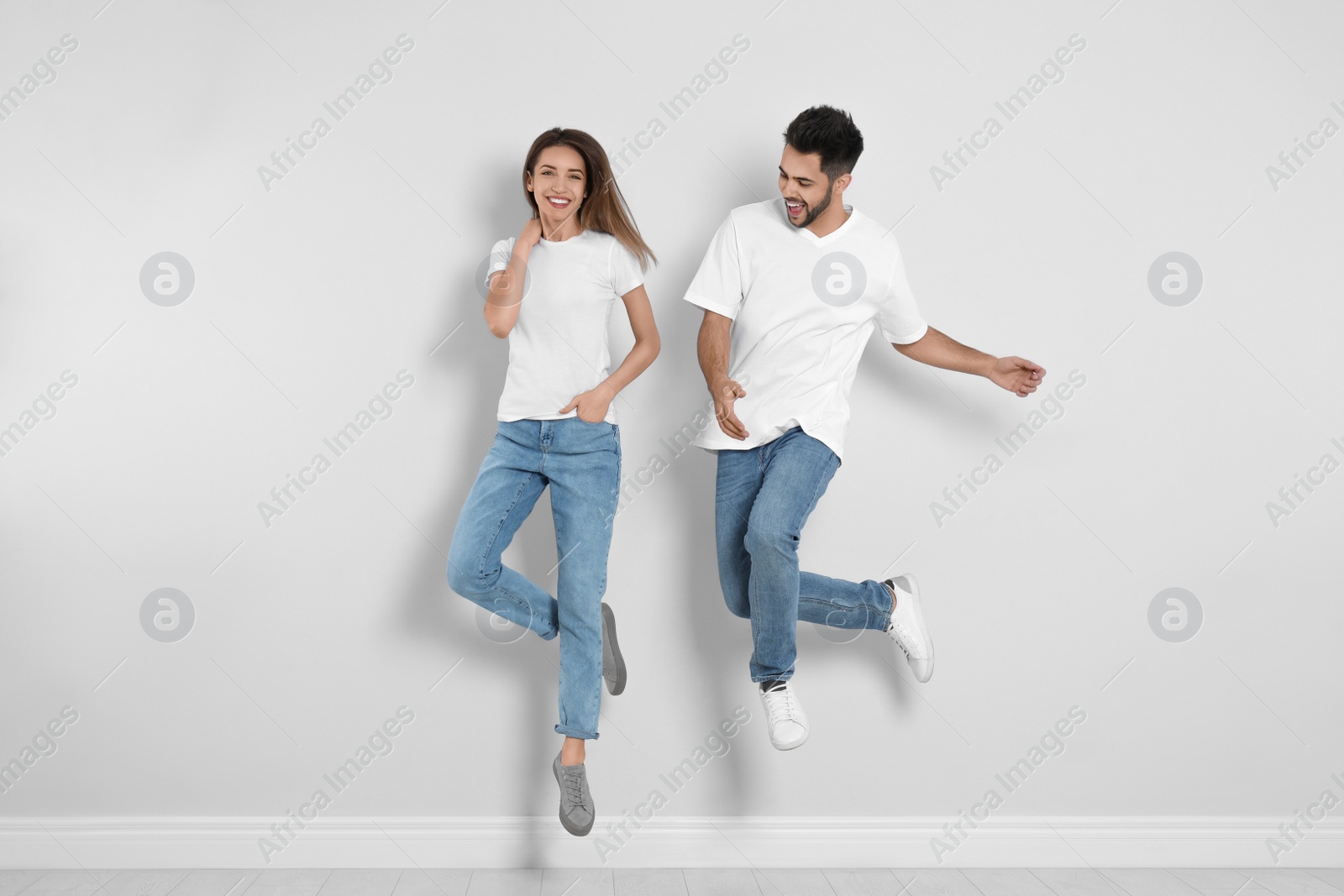 Photo of Young couple in stylish jeans jumping near light wall