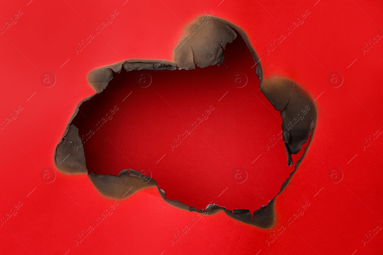 Photo of Burnt hole in paper on red background, space for text