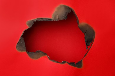 Photo of Burnt hole in paper on red background, space for text