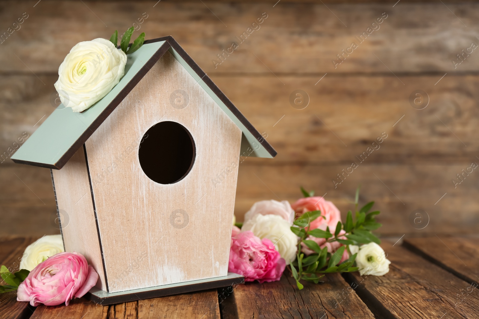 Photo of Stylish bird house and fresh eustomas on wooden table. Space for text