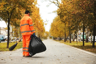 Photo of Street cleaner with broom and garbage bag outdoors on autumn day, back view