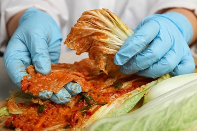 Photo of Woman preparing spicy cabbage kimchi at table, closeup