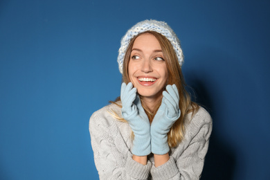 Happy young woman wearing warm sweater, knitted hat and mittens on blue background 