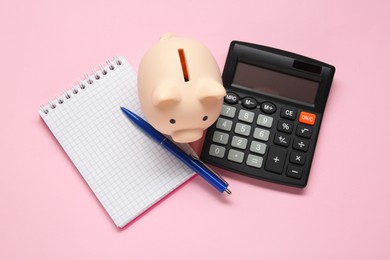 Calculator, piggy bank, pen and notebook on pink background, flat lay