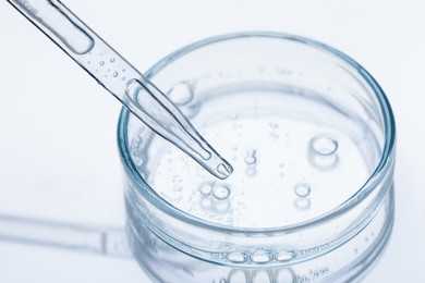 Photo of Glass pipette and petri dish with liquid on beige background, closeup