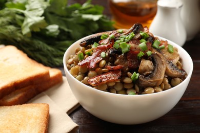 Photo of Delicious lentils with mushrooms, bacon and green onion in bowl served on table, closeup