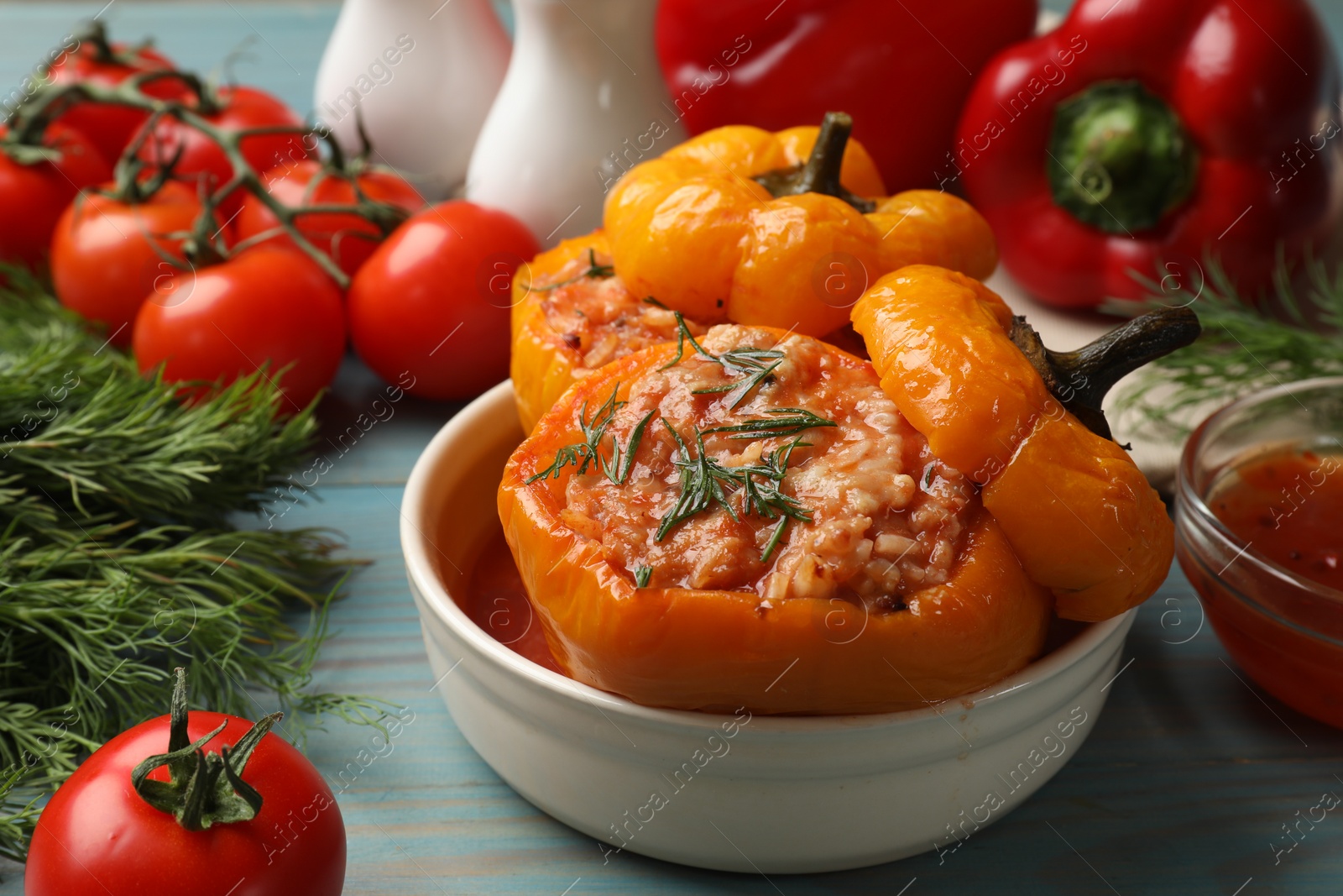 Photo of Tasty stuffed peppers in bowl and products on light blue wooden table, closeup