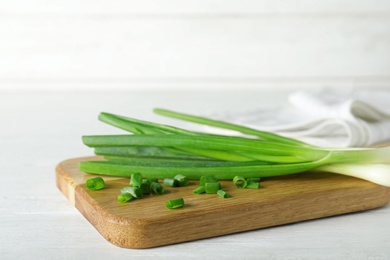 Photo of Wooden board with cut fresh green onions on white table. Space for text